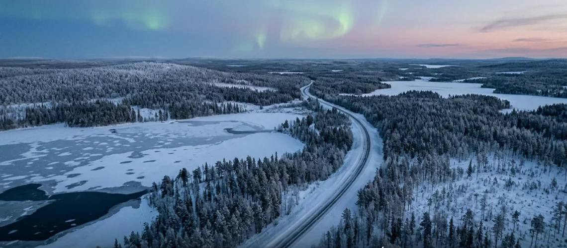 Vue aérienne de la Laponie enneigée au crépuscule avec forêt boréale et aurore verte